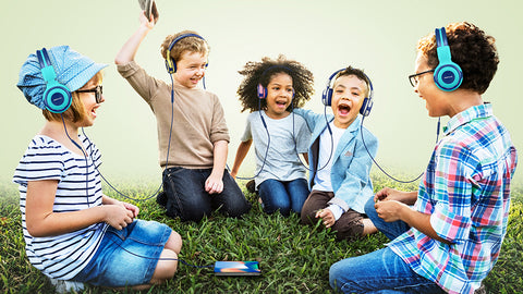 Five children sit together on grassland and use SIMOLIO kids headphones to share audio