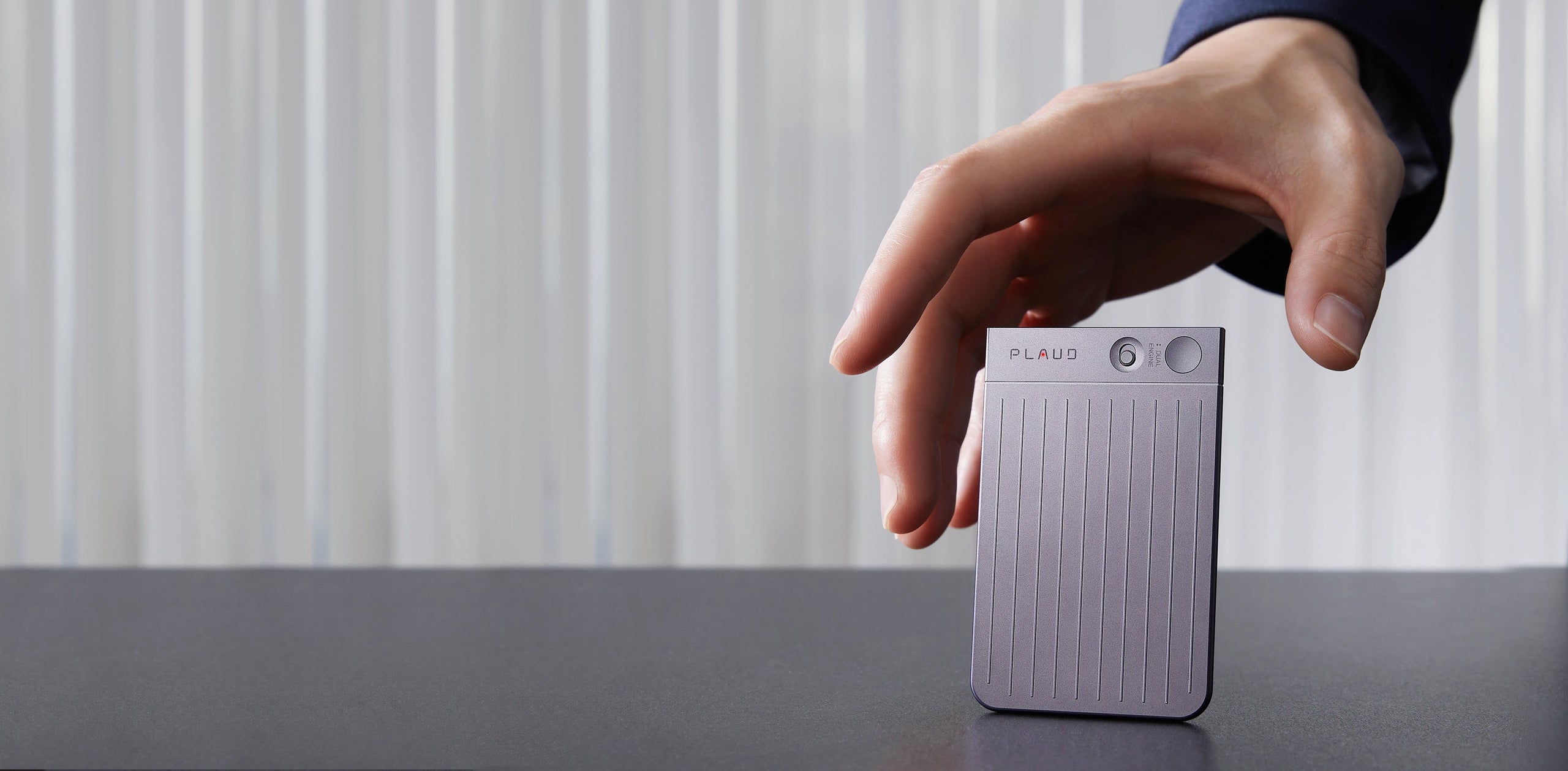A hand reaches to pick up a Starlight Plaud Note AI voice recorder from a dark desk.