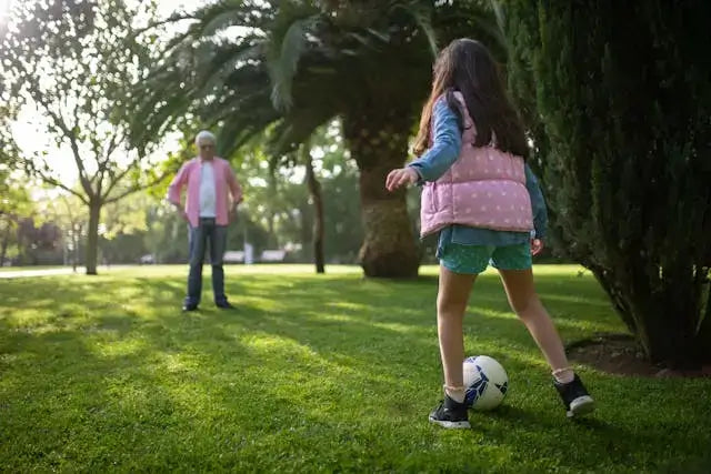 girl and her grandpa are playing football on the lawn