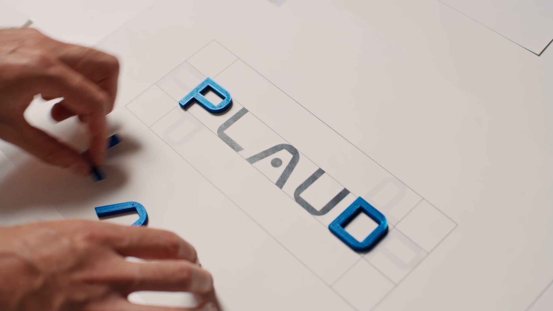 Plaudのブランドロゴを青い立体文字で組み立てる手元