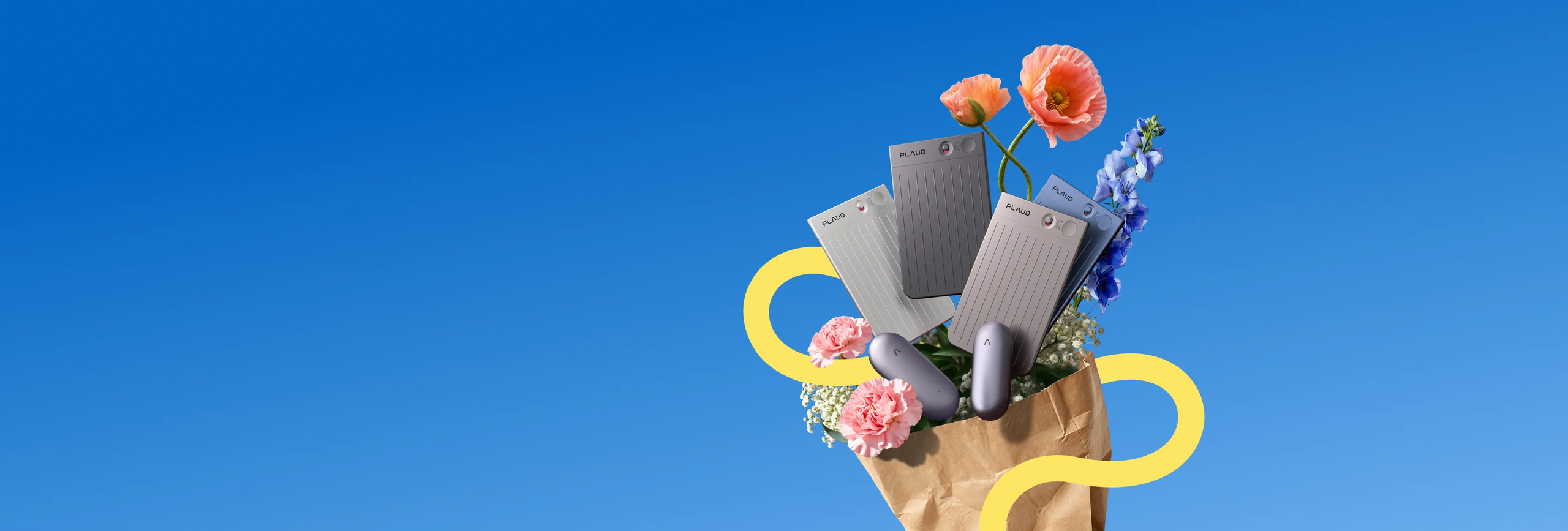 Several silver Plaud Note and Plaud NotePin devices are arranged with colorful flowers spilling from a brown paper bag agains