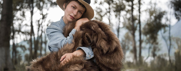 The model wearing a fluffy and warm brown faux fur blanket, which is multi-functional and easy to wash.