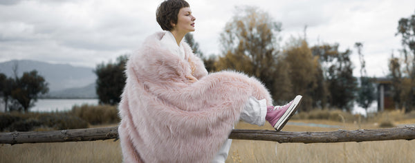 The model wearing a fluffy and plush pink faux fur blanket which is 100% cruelty-free and easy to wash.