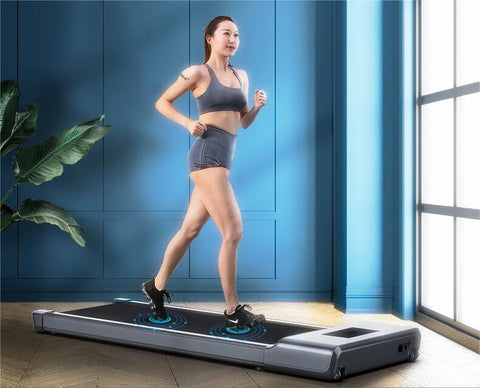 A woman exercising indoors on a gray treadmill. She is dressed in a black sports bra and shorts, paired with black sneakers. Blue indicator lights on the front of the treadmill display the speed and time. The background consists of a blue wall and a large window, through which green plants can be seen.