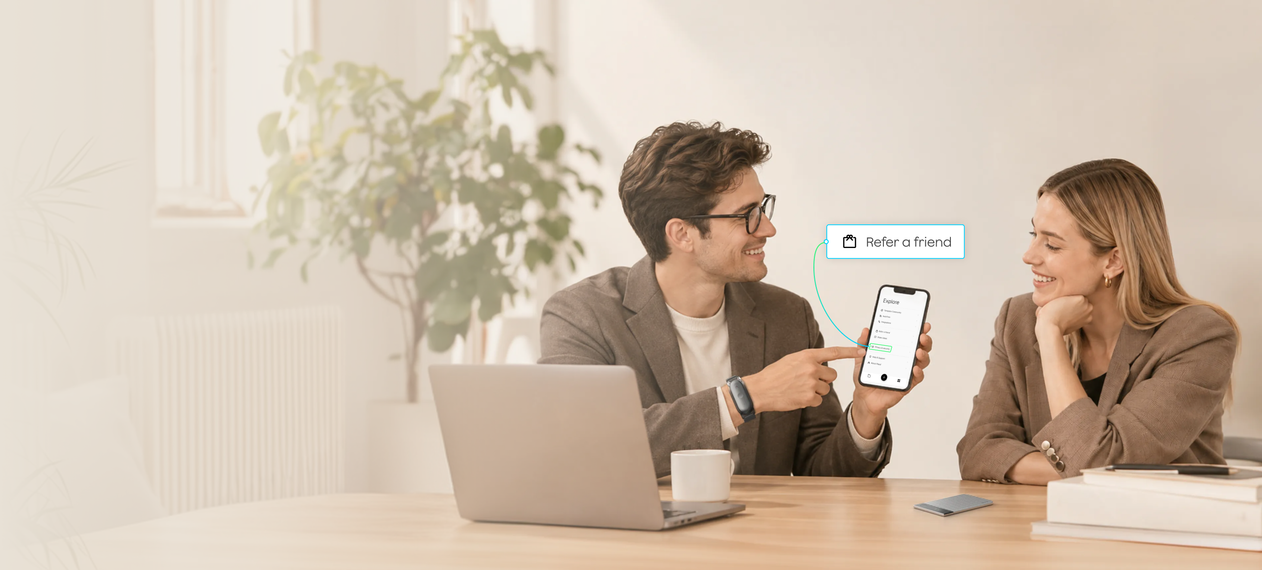 A man points to a Refer a friend callout for the Plaud App on his phone while wearing a black Plaud wearable AI recorder, with a silver Plaud AI voice recorder on the table.