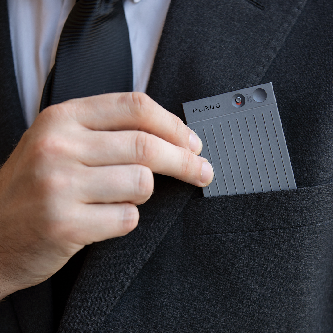 Professional in suit placing Plaud Note AI voice recorder in pocket, sleek gray design with vertical lines and Plaud logo