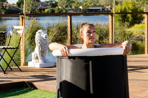 A woman enjoys a cold plunge in an outdoor setting, surrounded by a scenic environment.