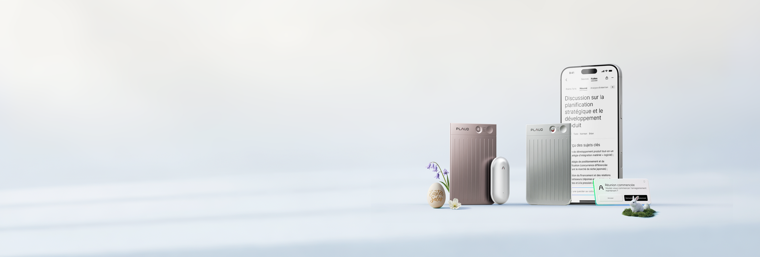 Deux Plaud Note (bronze et argent) et un Plaud NotePin blanc sont présentés avec un smartphone et des décorations printanière