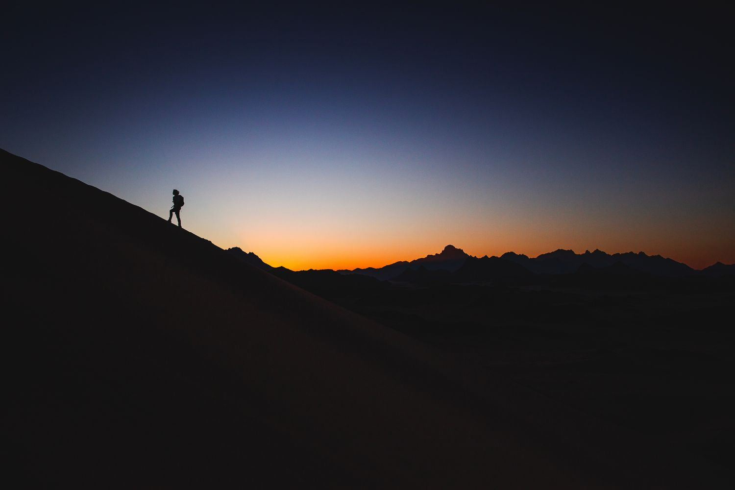 man is climbing a mountain alone in the sunset